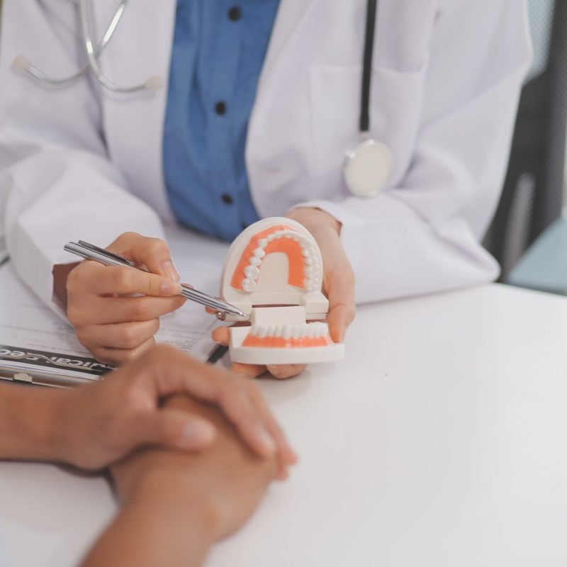 Dentist consultation - patient visit at the dental clinic office. Female dentist wearing dentures to explain teeth Recommend guidelines for orthodontics Dentist giving advice on patient's condition